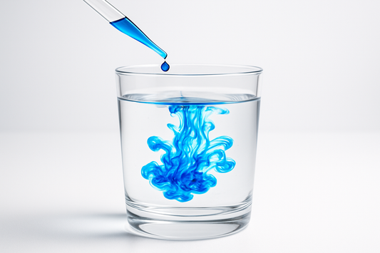 Methylenblau das mit einer Pipette in ein Kristallglas mit Wasser getropft wird 